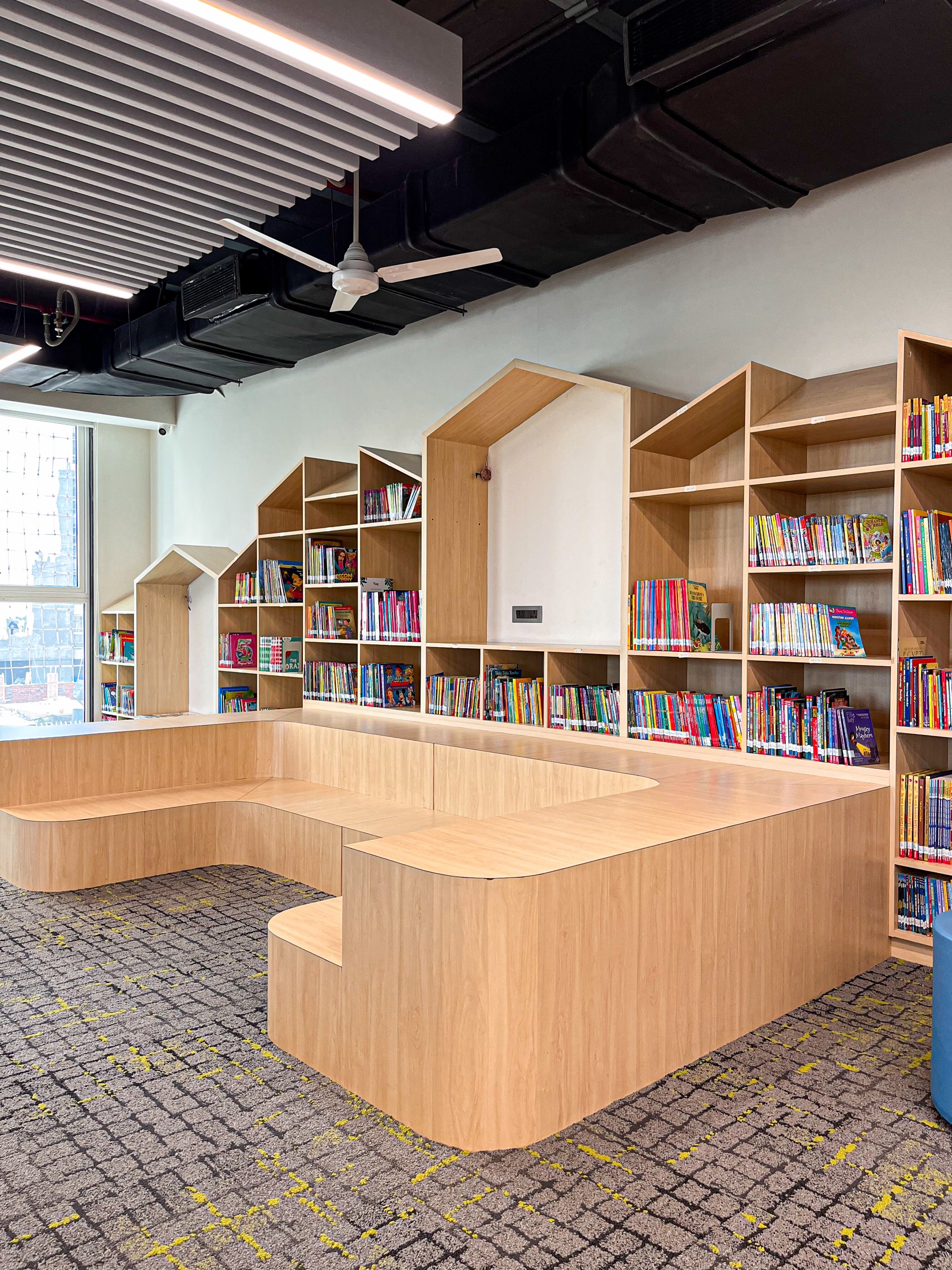 Sculptural house-shaped bookshelves around a curved reading bench