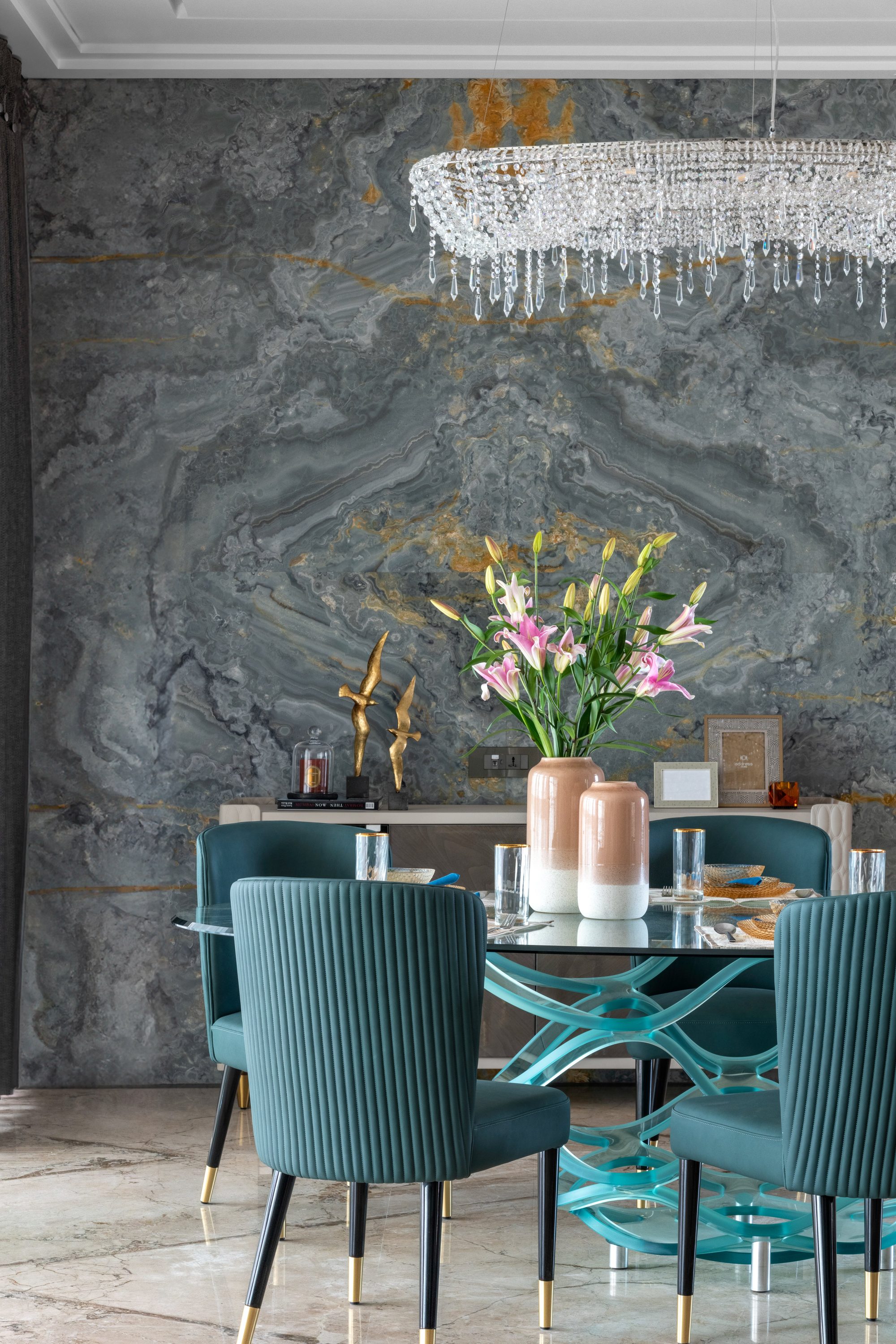 Dining table with teal velvet chairs against grey and gold marble wall